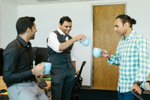 Three office colleagues talking and holding coffee mugs during a casual office break