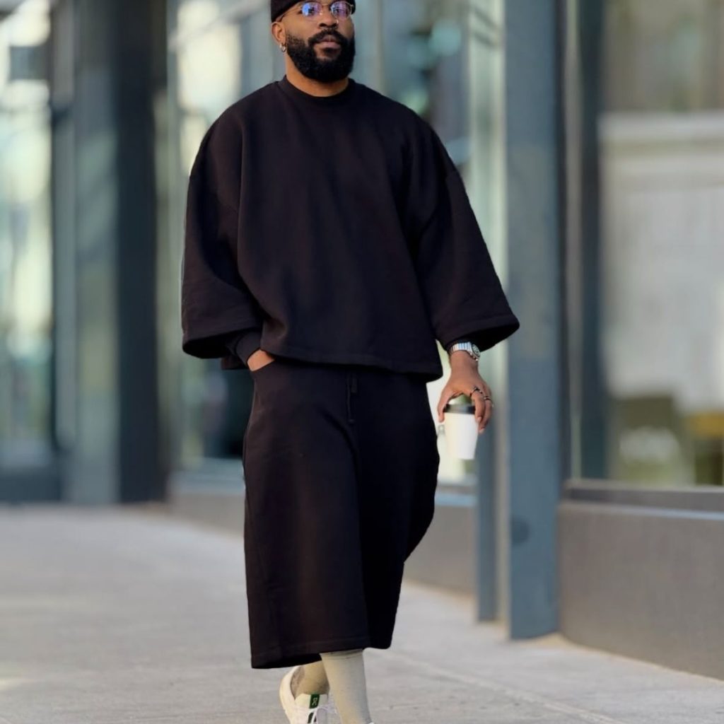 Man wearing oversized black streetwear outfit with wide shorts and sneakers in modern urban street style